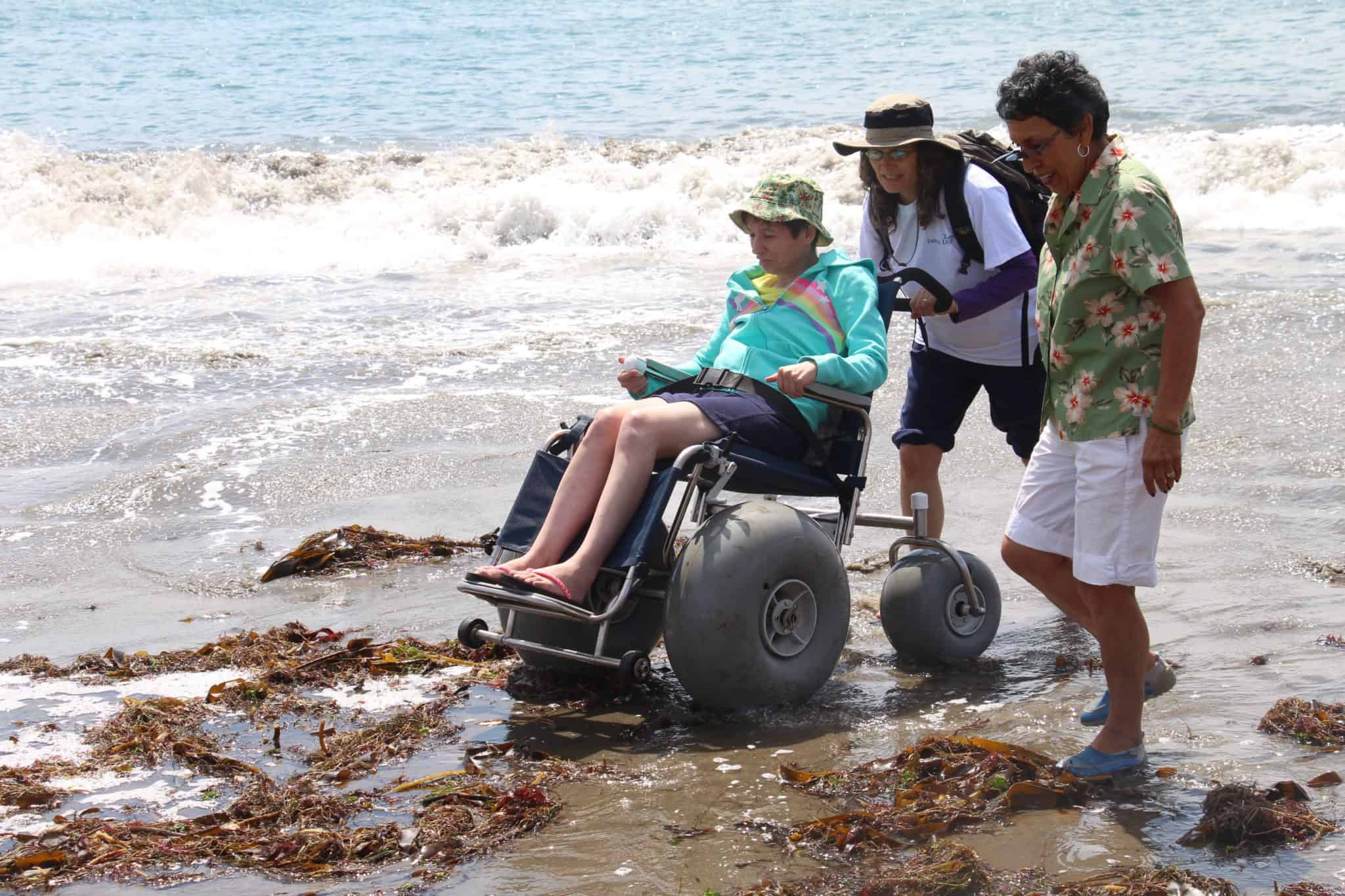 Women being pushed over the sand in a beach wheelchair